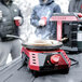 A group of people standing around a Mr. Heater Buddy FLEX portable liquid propane radiant cooker on a table outdoors.