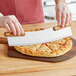 A person using a Fox Run stainless steel pizza rocker knife to cut a slice of pizza.