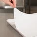 A hand using a Baker's Lane parchment paper sheet to line a baking sheet.