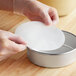 A person wearing gloves uses a Baker's Lane round silicone pan liner to line a round cake pan.