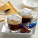 Two glass cups of ALMOND JOY Cappuccino with whipped cream and chocolate on a white plate.
