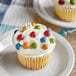 A cupcake with frosting and Natural Rainbow Chocolate Gems on top.