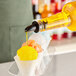 A bottle of yellow Hawaiian Shaved Ice syrup being poured into a small cone