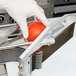 A person in gloves uses a Vollrath Redco Tomato Slicer to cut a tomato.