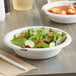 A Dixie Ultra Pathways paper bowl filled with salad on a wood table.