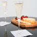 Two Stolzle flute glasses of champagne on a table with a plate of strawberries.