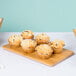 A rectangular American Metalcraft bamboo platter with muffins on a table.