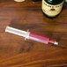 A Jell-O injector filled with red liquid next to a bottle.