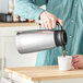 A person pouring coffee into a Bunn stainless steel thermal pitcher.