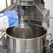 An Avantco floor mixer with a wire whisk attachment mixing a bag of flour.