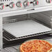 A Nemco pizza stone with a pizza cooking in a countertop oven.
