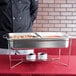 A chef using a Vollrath stackable wire chafer stand to serve food on a large tray.
