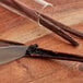A knife cutting a vanilla bean on a wooden table.