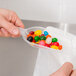 A person holding a Fineline clear plastic utility and ice scoop full of jelly beans.