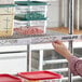 A hand holding a label in a clear label holder on a shelf with containers of food.