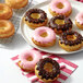 A white plate with Wilton donut pans filled with donuts frosted with chocolate and pink icing and sprinkles.