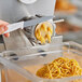 A hand using a knife to cut noodles with an Estella spaghetti pasta die on a pasta machine.