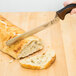 A brown handled Mercer Culinary Millennia Colors knife cutting a piece of bread.