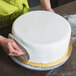 A person using an Ateco plastic fondant smoother to decorate a white cake.