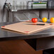 A San Jamar brown cutting board on a counter with a knife and fruit.
