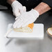 A person in white gloves cutting a bun on a white San Jamar bar size cutting board.