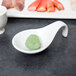 A white porcelain tapas spoon with green food on it.