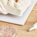 A hand using placing a white cake on a Baker's Lane white cake drum.