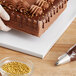 A person using a gloved hand to place a white cake on a Baker's Lane cake drum.