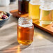 A small glass mason jar filled with a golden beverage, shown on a wooden table.