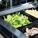A Vollrath black polycarbonate food pan with food in it including chicken, lettuce, and eggs on a counter in a buffet.