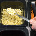 A hand using an American Metalcraft stainless steel spoon to serve corn from a container.