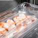 A Vollrath clear polycarbonate food pan filled with shrimp on a counter.