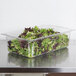 A clear plastic Vollrath food pan filled with lettuce on a counter.