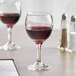Two Acopa balloon wine glasses filled with red wine on a table with a menu.