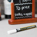 An American Metalcraft white chalk marker sits on a blackboard with white writing on it.