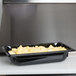 A black rectangular Vollrath polycarbonate food pan with scrambled eggs in it.