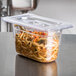 A Vollrath 1/9 size clear polycarbonate plastic lid on a plastic container with noodles and vegetables in it.