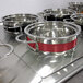 A Bon Chef Classic Country French red steam table pot in a group of metal pots.