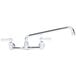 A chrome Advance Tabco wall-mount faucet with two handles and a 12 1/8" swing nozzle.