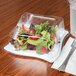 A salad in a clear plastic container with a clear dome lid on a table.