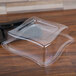 A clear plastic container with a clear dome lid on a wood table.