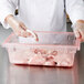 A person in gloves putting meat into a Carlisle red food storage box.