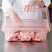 A person in a plastic glove holding a Carlisle red food storage container with raw meat.