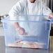 A chef in a white coat putting raw fish in a Carlisle blue plastic food storage container.