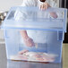A chef wearing gloves uses a Carlisle blue food storage box to hold raw fish.