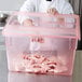 A person in a white shirt and gloves holding a Carlisle red plastic food storage container with raw meat in it.
