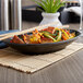 A black Elite Global Solutions Zen oval plate with food and chopsticks on a table.