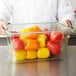 A chef in a white coat holding a Carlisle green food storage container of yellow and red bell peppers.