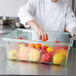 A chef wearing a white coat and gloves putting an orange bell pepper into a Carlisle green food storage box.