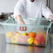 A chef in a white coat and gloves putting yellow, orange, and red bell peppers in a Carlisle green food storage box.
